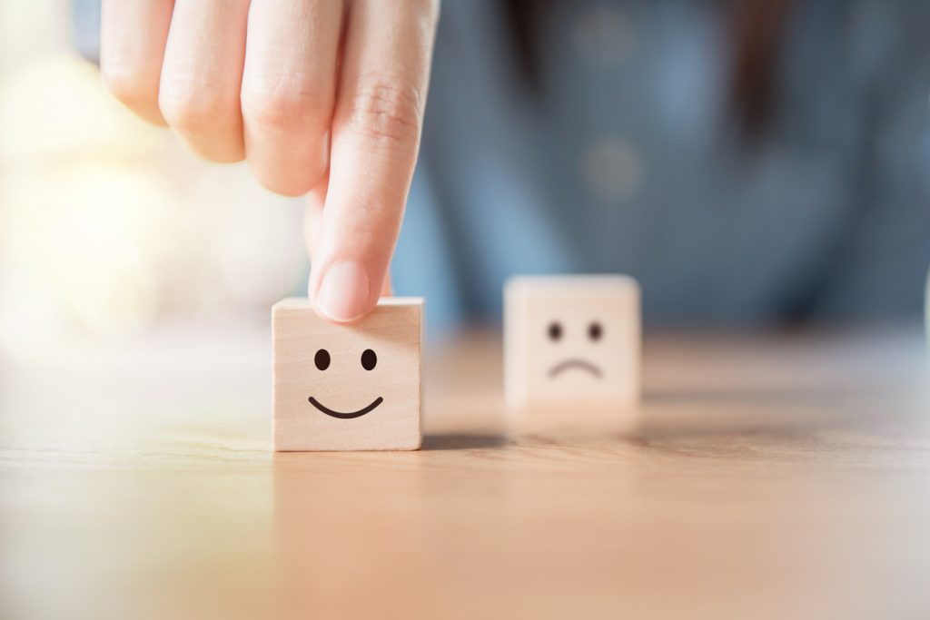 Close up hand choose smiley face and blurred sad face icon on wood cube, Service rating, satisfaction concept.